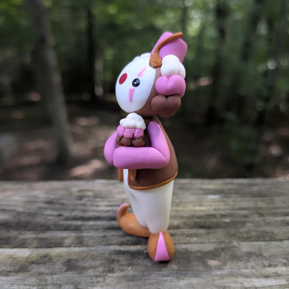 A Neapolitan ice cream themed clown sculpture. He is outfit is pink, brown, and white. He wears golden Khussa slippers and a pink Tarboosh. He holds a triple stacked ice cream cone.