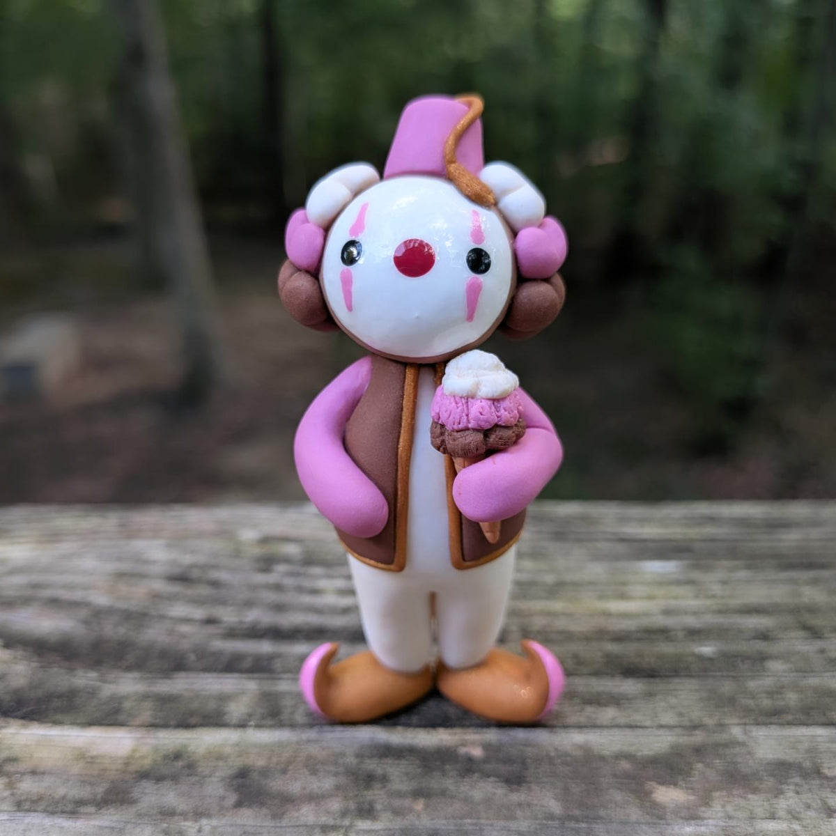 A Neapolitan ice cream themed clown sculpture. He is outfit is pink, brown, and white. He wears golden Khussa slippers and a pink Tarboosh. He holds a triple stacked ice cream cone.