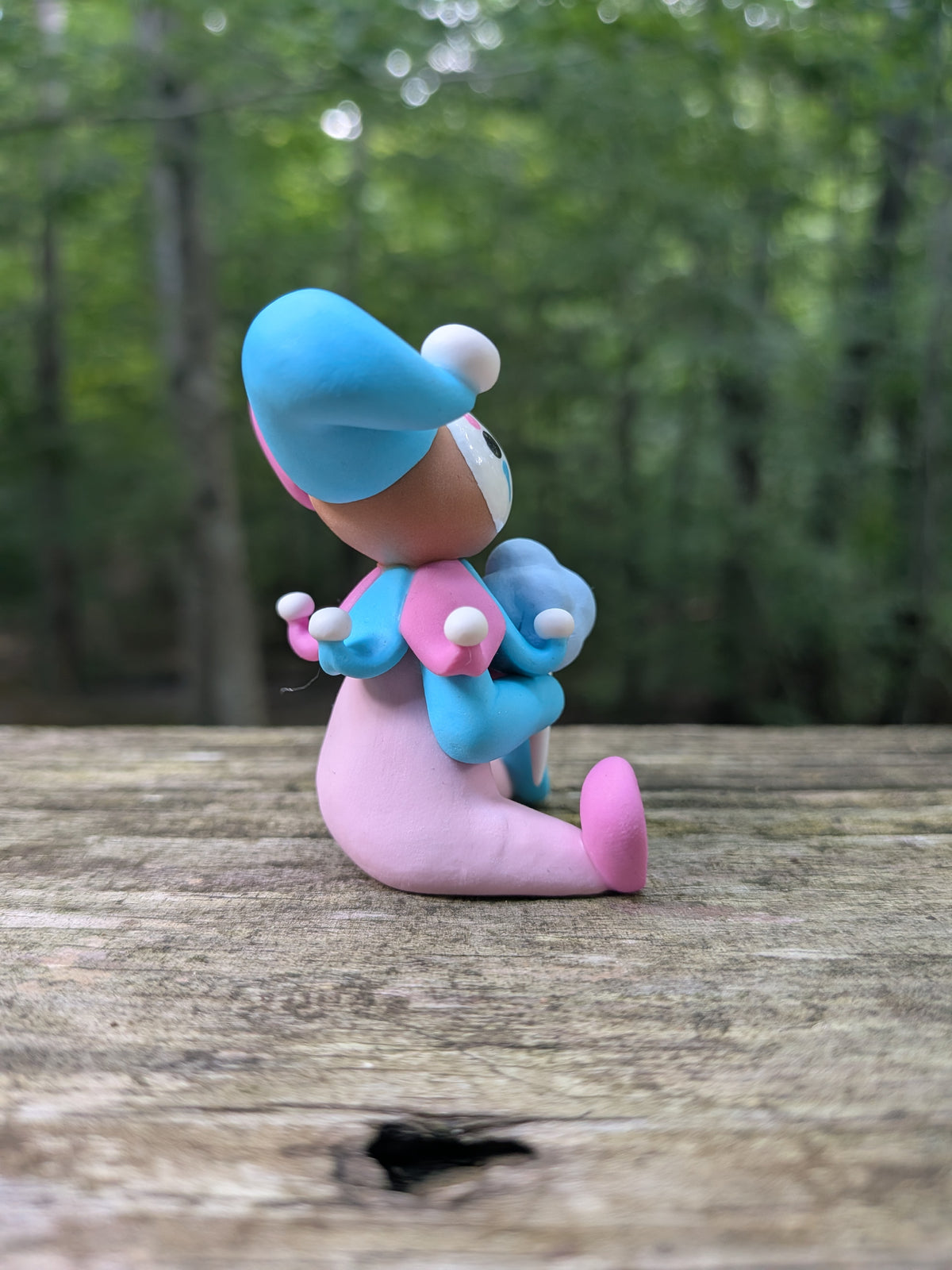 A sculpture of a pink and blue jester clown sitting with a blue cotton candy. He has alternating pink and blue elements and a big jester hat.