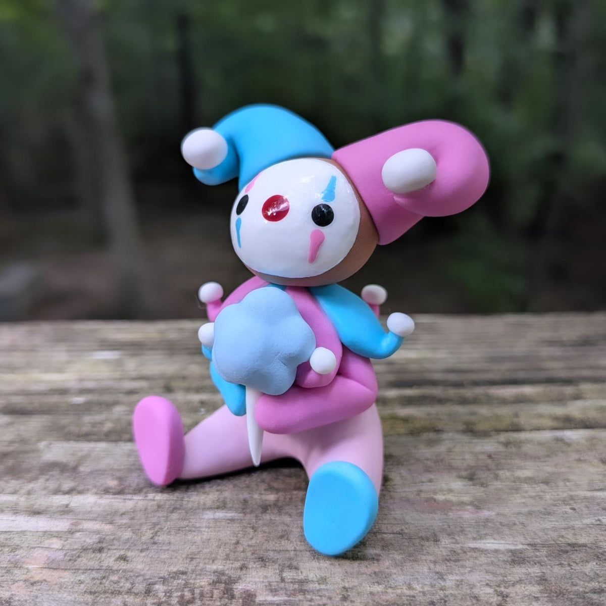 A sculpture of a pink and blue jester clown sitting with a blue cotton candy. He has alternating pink and blue elements and a big jester hat.