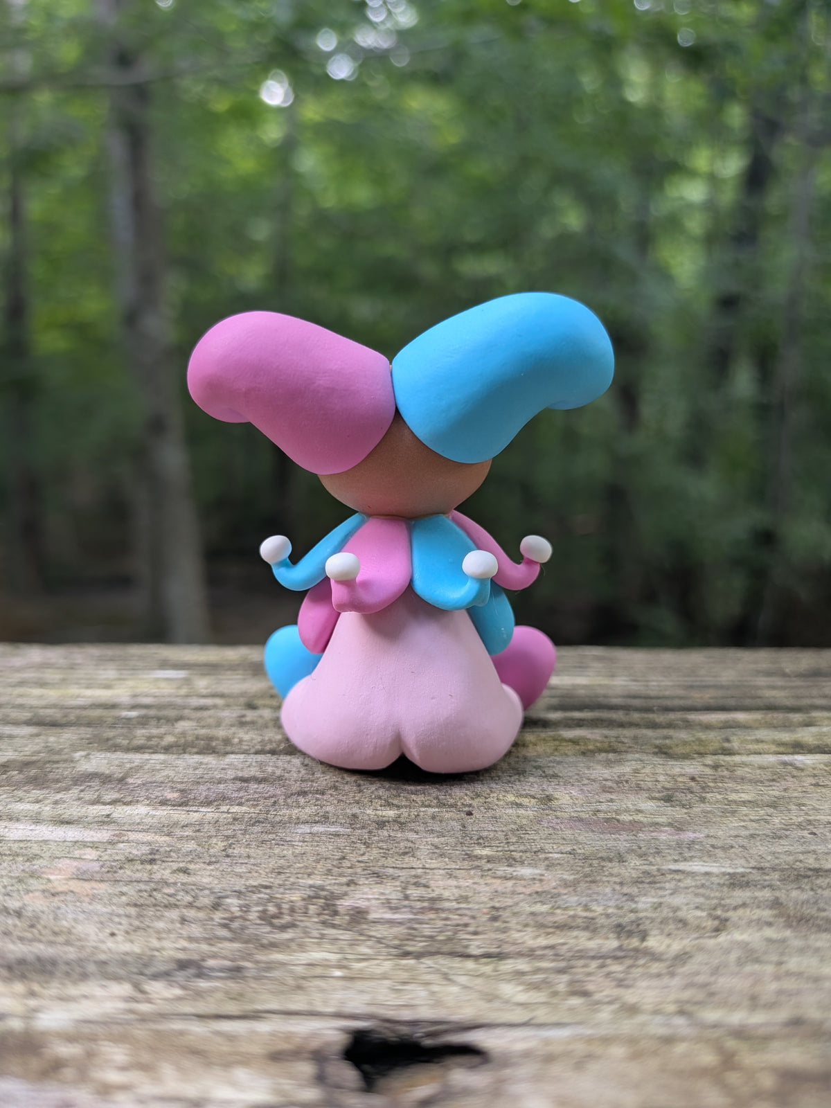 A sculpture of a pink and blue jester clown sitting with a blue cotton candy. He has alternating pink and blue elements and a big jester hat.