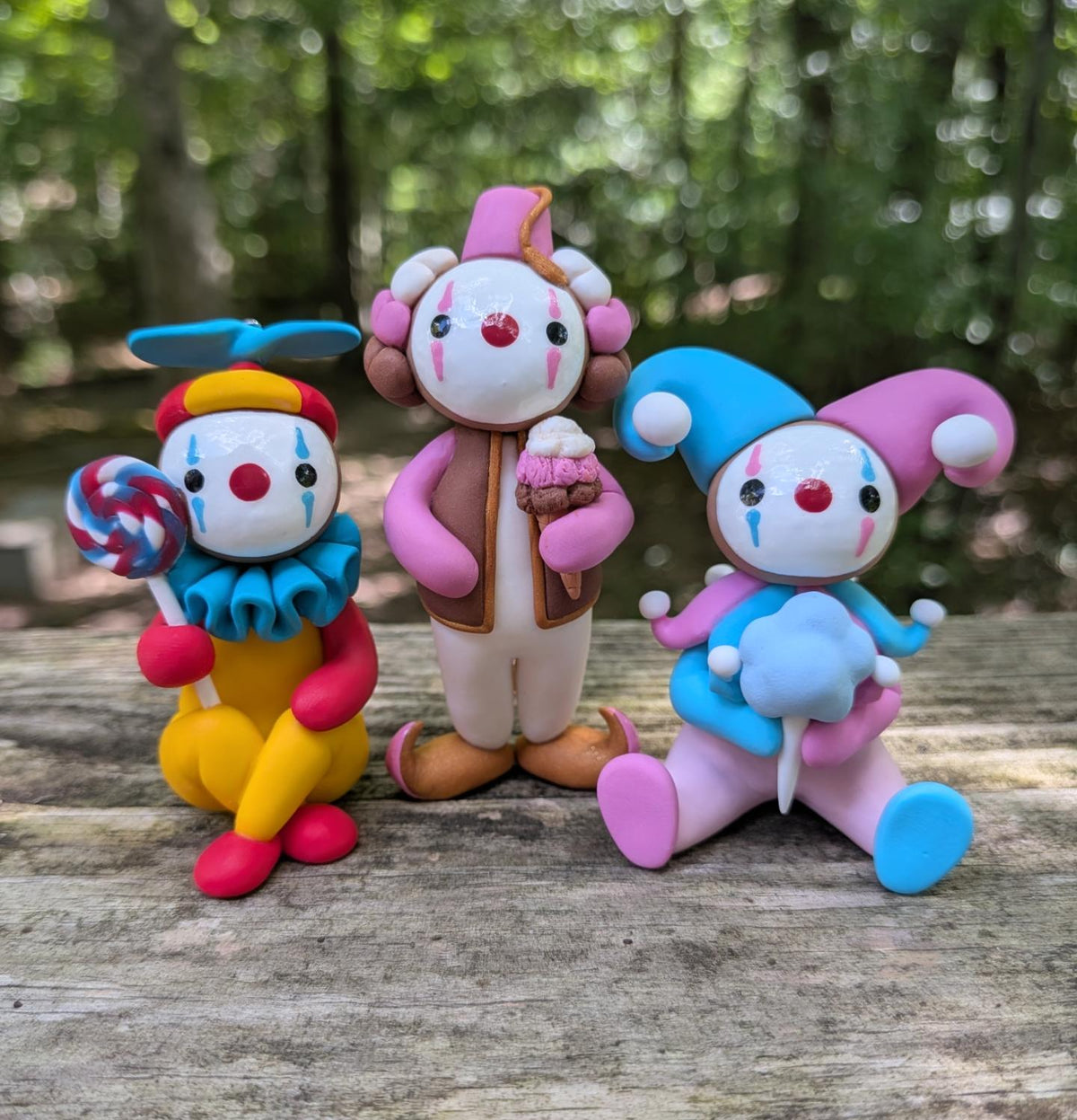 Three colorful clown sculptures. The left clown is yellow, red, blue and holding a big lollipop. The middle clown is Neapolitan themed and is holding an ice cream cone. The right clown is pink and blue holding cotton candy.