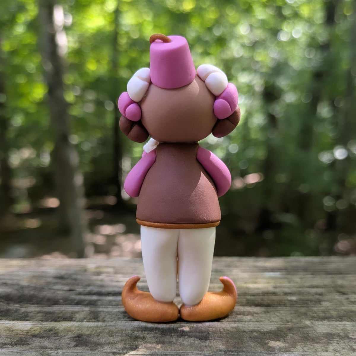 A Neapolitan ice cream themed clown sculpture. He is outfit is pink, brown, and white. He wears golden Khussa slippers and a pink Tarboosh. He holds a triple stacked ice cream cone.