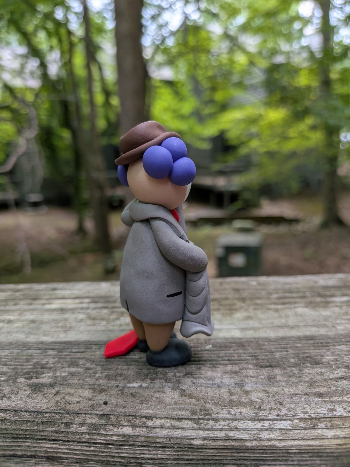 A back right view of a clown in oversized business attire. You can see his long sleeves and a hint of a his tie dragging on the ground. He has purple hair that is bald down the middle.