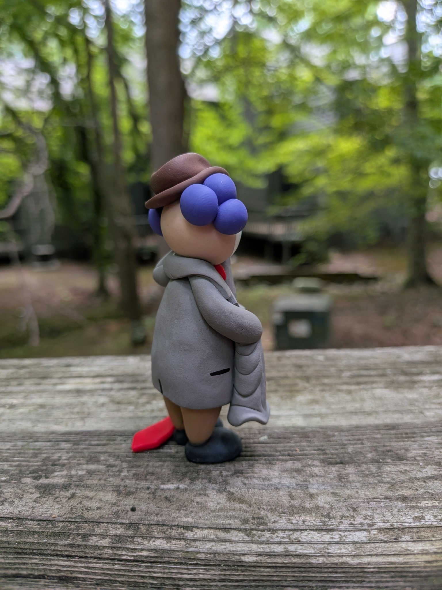 A back right view of a clown in oversized business attire. You can see his long sleeves and a hint of a his tie dragging on the ground. He has purple hair that is bald down the middle.