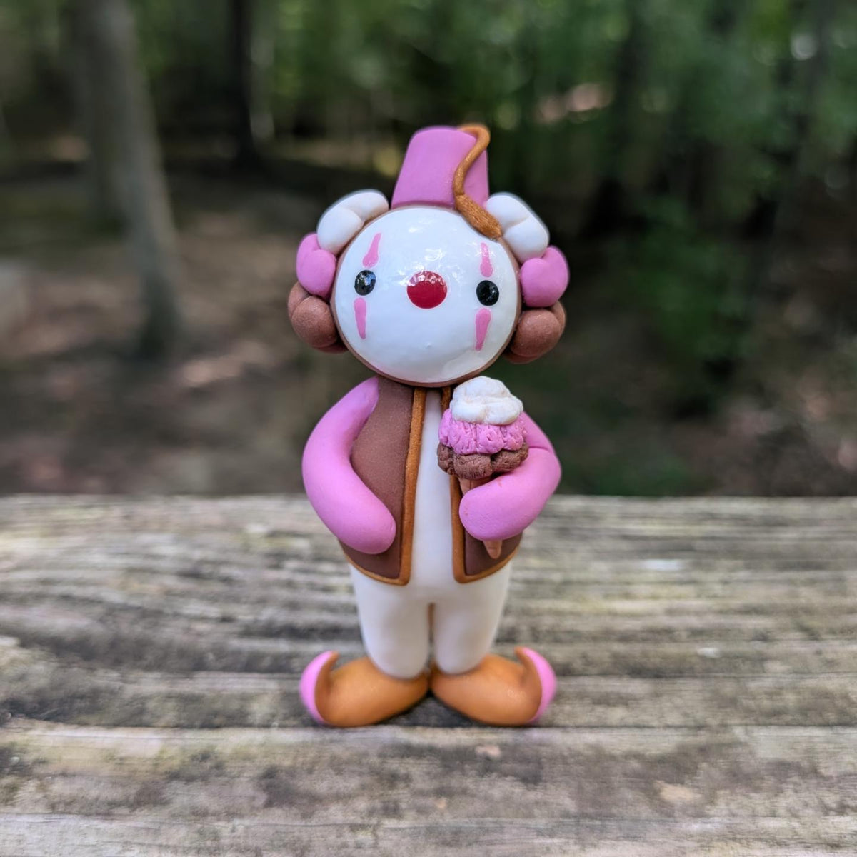 A Neapolitan ice cream themed clown sculpture. He is outfit is pink, brown, and white. He wears golden Khussa slippers and a pink Tarboosh. He holds a triple stacked ice cream cone.