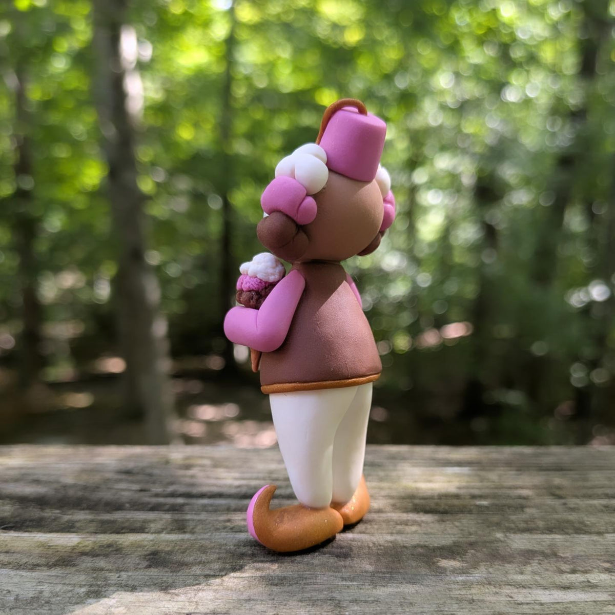 A Neapolitan ice cream themed clown sculpture. He is outfit is pink, brown, and white. He wears golden Khussa slippers and a pink Tarboosh. He holds a triple stacked ice cream cone.