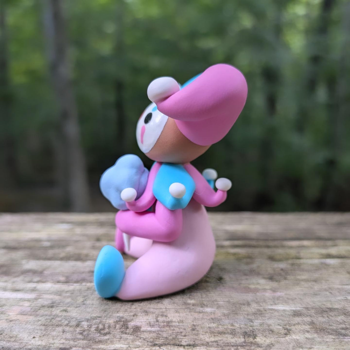 A sculpture of a pink and blue jester clown sitting with a blue cotton candy. He has alternating pink and blue elements and a big jester hat.