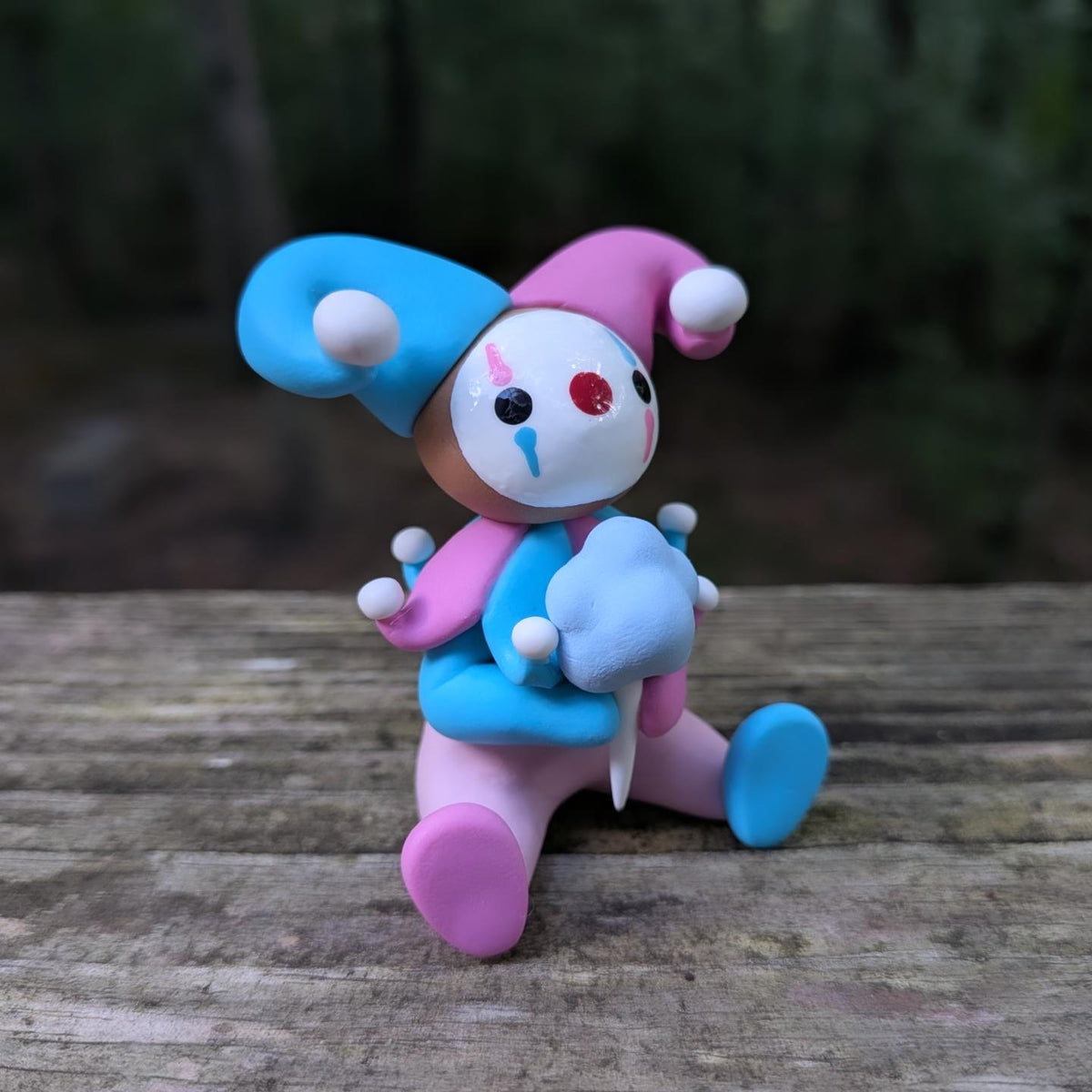A sculpture of a pink and blue jester clown sitting with a blue cotton candy. He has alternating pink and blue elements and a big jester hat.